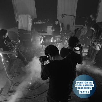 Eine Band wird von zwei Filmern aufgenommen mit Kameras