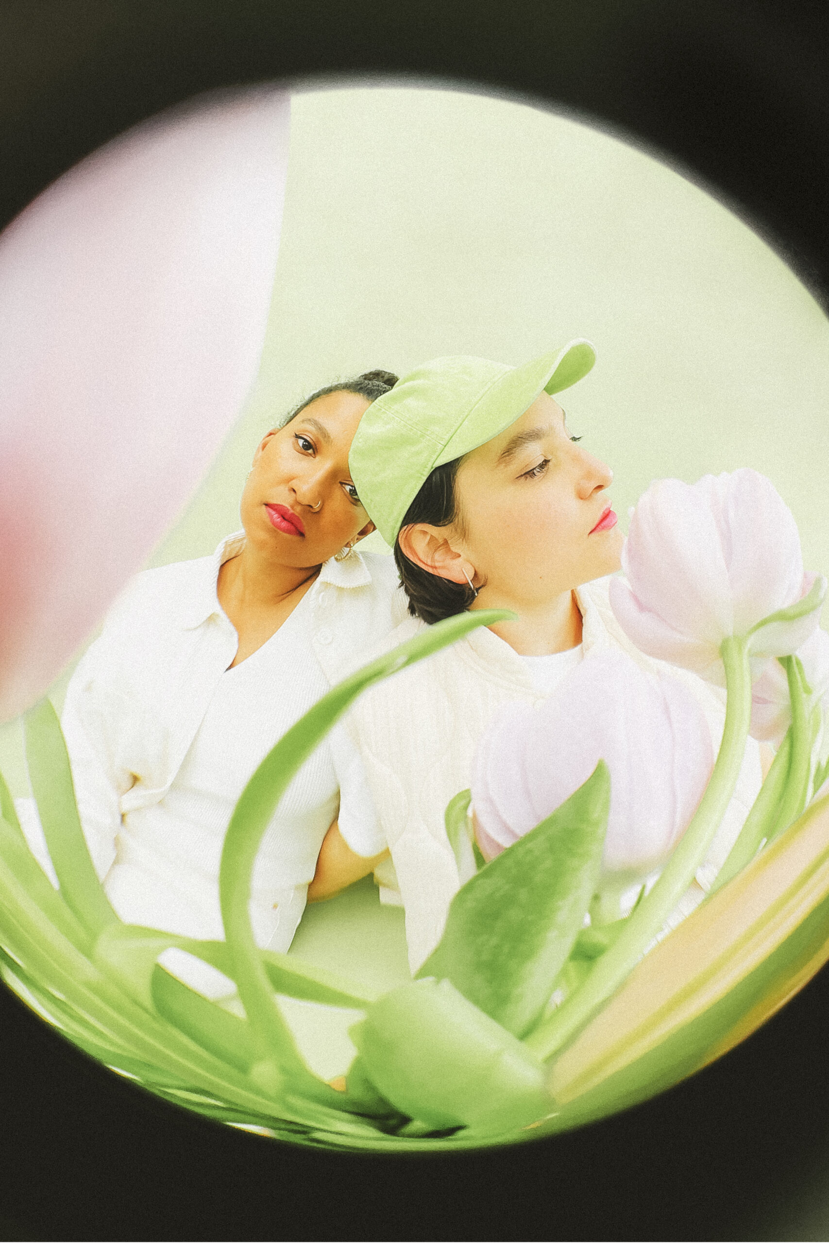 Zwei Frauen mit pinkem Lippenstift in einem hellgrünen Kreis mit Tulpen im Vordergrund