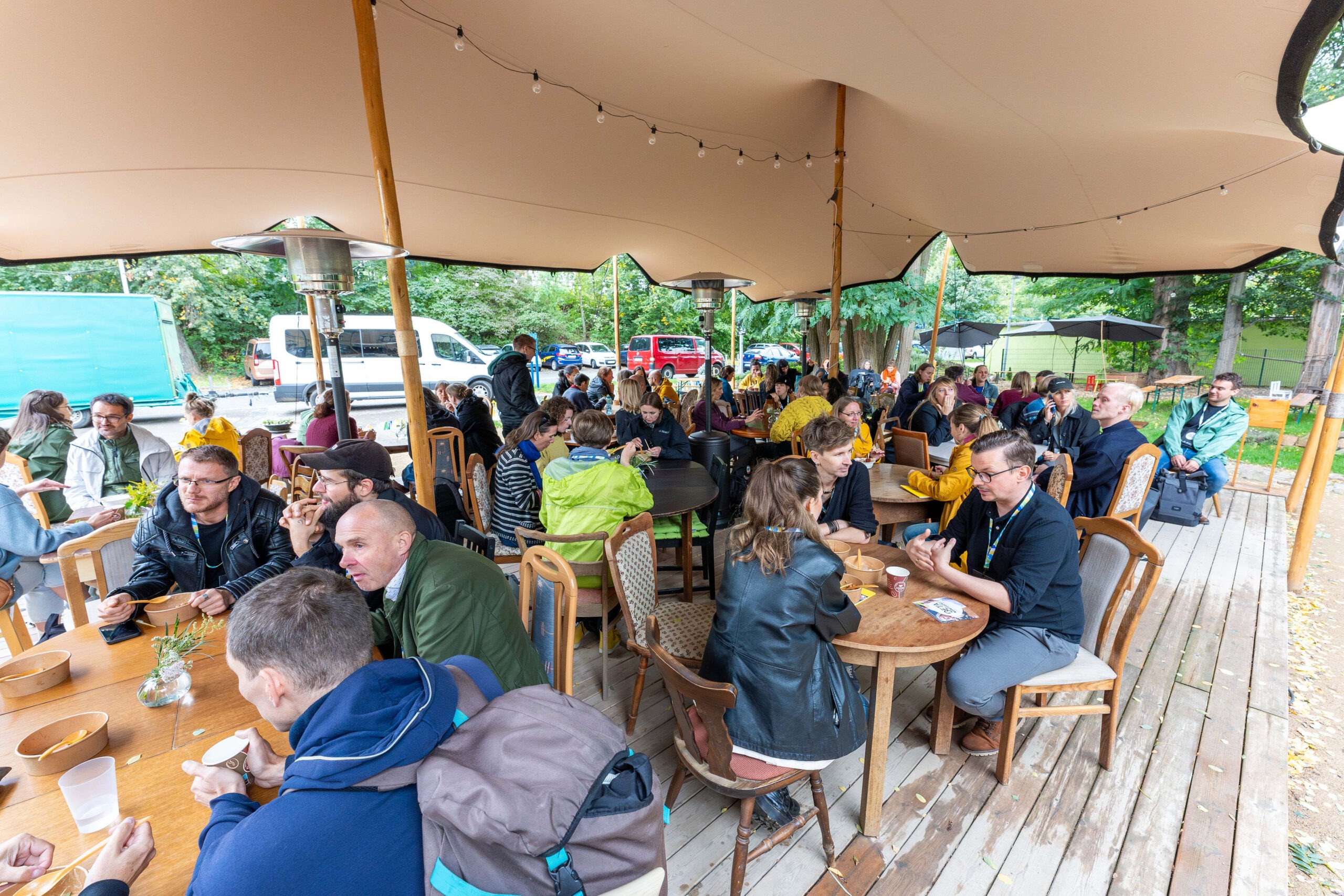 Ein großes Zeltdach, darunter viele Tische und Stühle auf denen Menschen sitzen und essen.